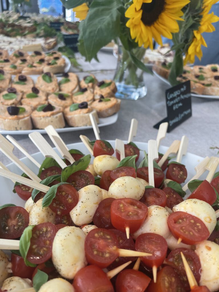 Ansicht eines Buffets mit Tomate-Mozzarella-Spießen, Häppchen und Sonnenblumen.